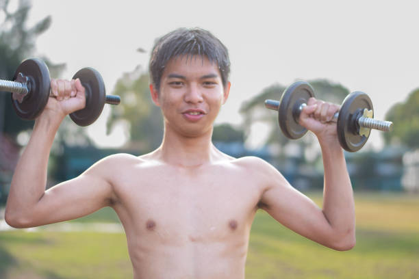 Asian teenager with dumbbell lifting at local park in late afternoon, loose weight and bodybuilding of teens concept.