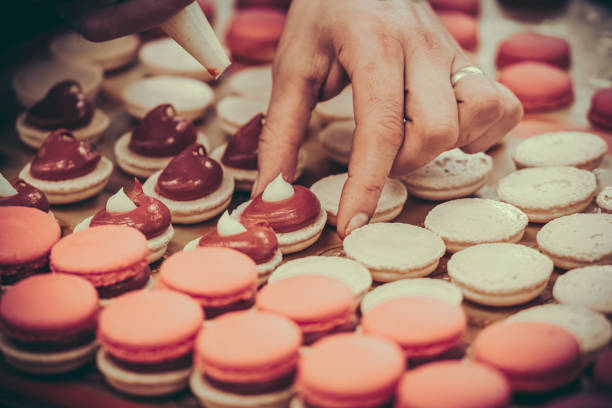 istock Confectioner's hands filling macarons with pink ganache cream 2152163037