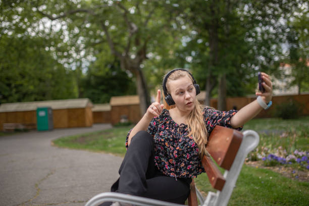 Young college girl sitting on a bench in the park and taking selfie with her phone