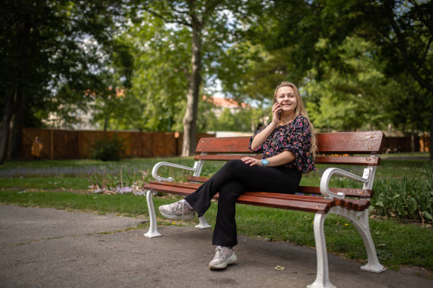 istock Young woman sitting in the park on a bench and using her smart phone 2152165265