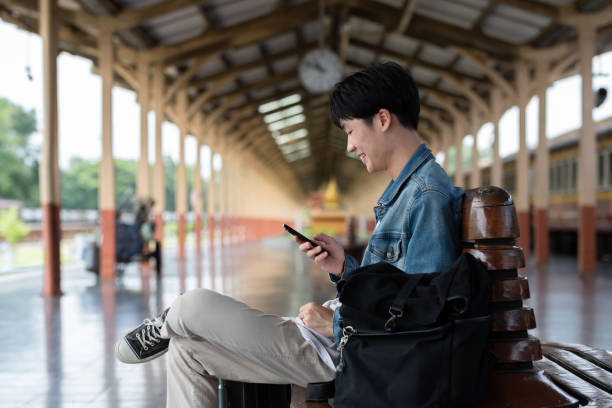 istock Young man with backpack checking social media on phone waiting for train at train station to travel 2152166017