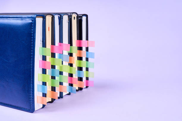 A stack of office notepads with colorful sticky page markers sandwiched between pages on purple background