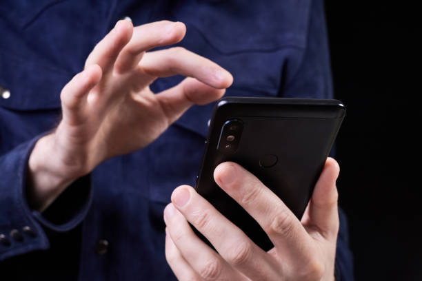 istock Man presses his finger on the screen of a smartphone on a dark background 2152166720