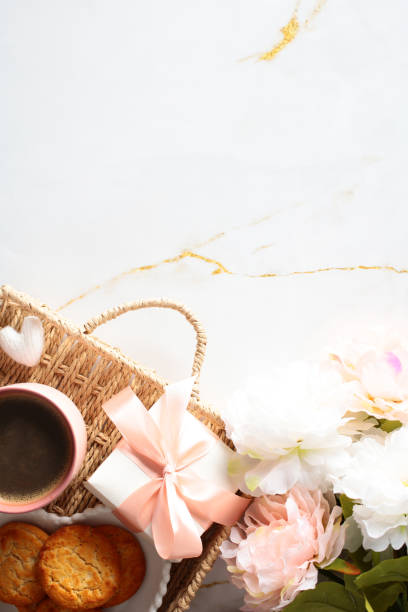 istock Wicker tray with coffee cup, gift box, cookies, flowers on marble desk. Top view. 2152173813