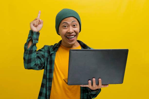 istock Happy young Asian man is working on a laptop and pointing a finger at empty copy space 2152173895