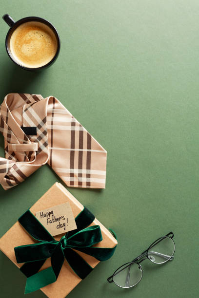 istock Happy Fathers Day banner design. Flat lay vertical composition with necktie, coffee cup, glasses, gift box with green ribbon bow on dark green background. 2152174184