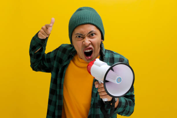 istock Angry Asian Man Yells into Megaphone, Demanding Change or Protesting, Isolated on Yellow Background 2152175439