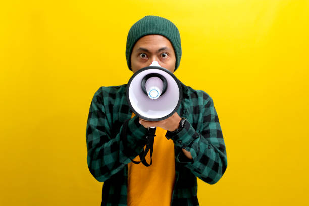 istock Angry Young Asian Man Shouts into Megaphone Against Yellow Background 2152175617