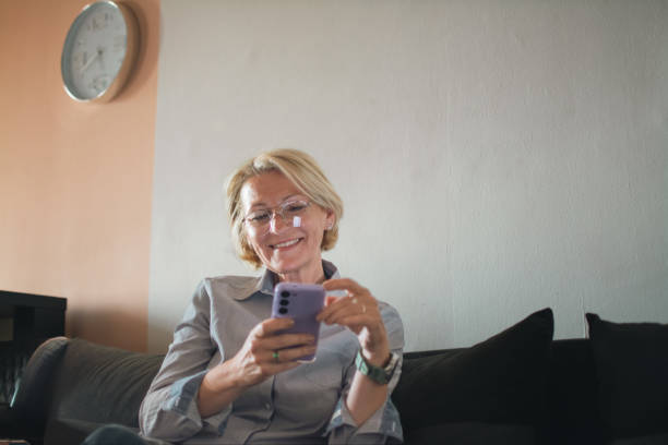 istock mature blond woman sitting on sofa and using mobile phone 2152176197