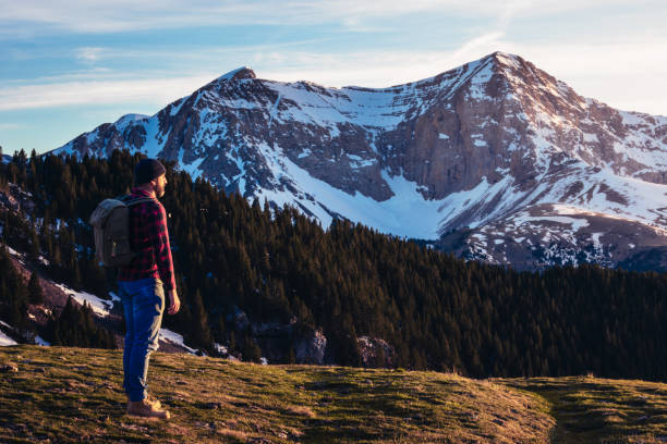 istock A man stands surrounded by high mountains and forests. The man carries a backpack and enjoys the view of the landscape. 2152176770