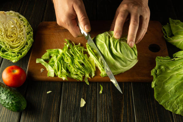 istock Chef hands with a knife while cooking on a kitchen black table. Delicious salad for breakfast with fresh vegetables by the hands of the cook 2152180482