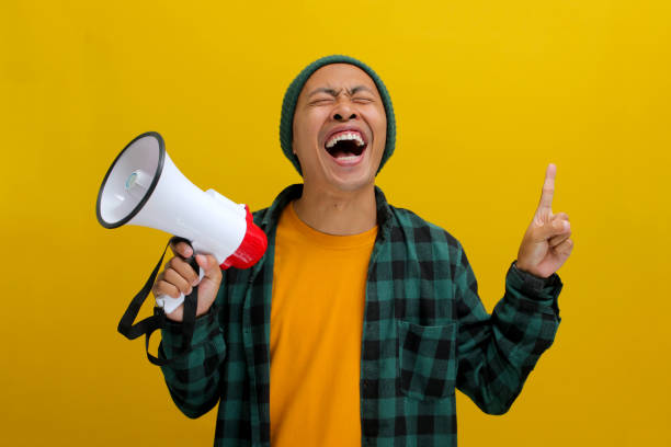 istock Happy Asian Man in Beanie Talks into Megaphone, Points to Copy Space for Discount Promotion or Sale 2152181332
