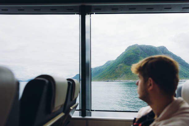 Silhouette of a male traveler sitting on the ferry boat seat and crossing the ocean with scenic summer fjord view in Norway, Scandinavia