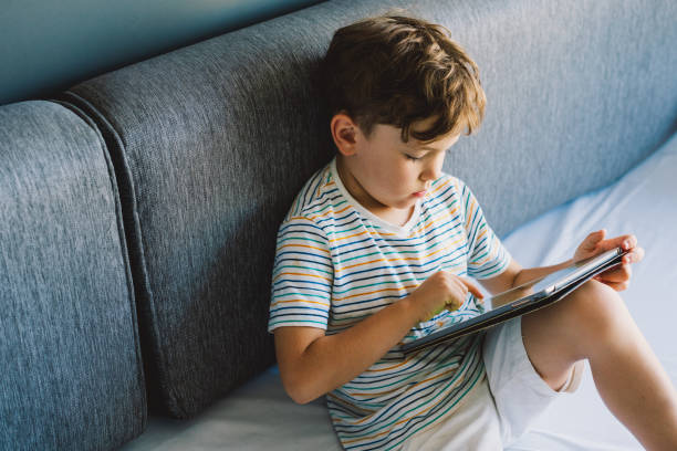 istock Young Boy Engrossed in playing tablet on a Cozy Couch During Afternoon Hours 2152185489