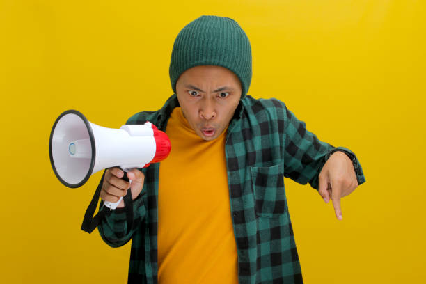 istock Happy Asian Man in Beanie Talks into Megaphone, Points to Copy Space for Discount Promotion or Sale 2152191369