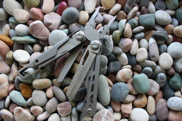 Universal camping folding tool kit with file, saw, metal knife and pliers on a smooth stones surface