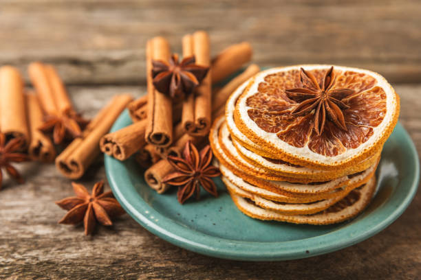 Scented spices: dried orange slices, vanilla beans, cinnamon, star anise and nutmeg shot on rustic wooden table. Predominant colors are orange, green and brown. High resolution 42Mp studio digital capture taken with SONY A7rII and Zeiss Batis 40mm F2.0 CF lens