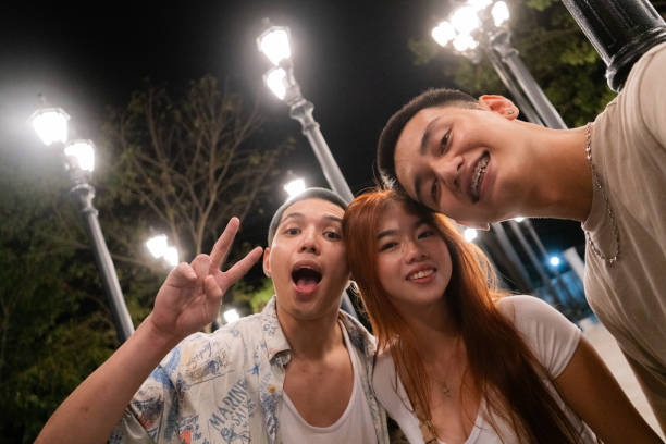 Three people are in the photo. They are all smiling. The woman is on the middle, wearing a white shirt. The man in the left is wearing a white shirt and has braces. The man on the right is wearing a blue shirt with white and yellow flowers.