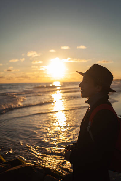 istock Tranquil man strolls beach under vibrant sunset hues. 2152204187