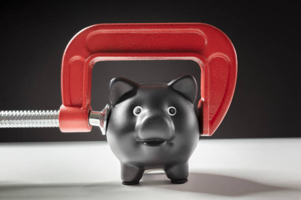 Piggy bank being squeezed by red clamp concept for recession, bankruptcy, debt, cheap and financial problems