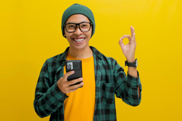 istock Asian man makes an OK sign gesture towards the camera while holding a phone 2152209394