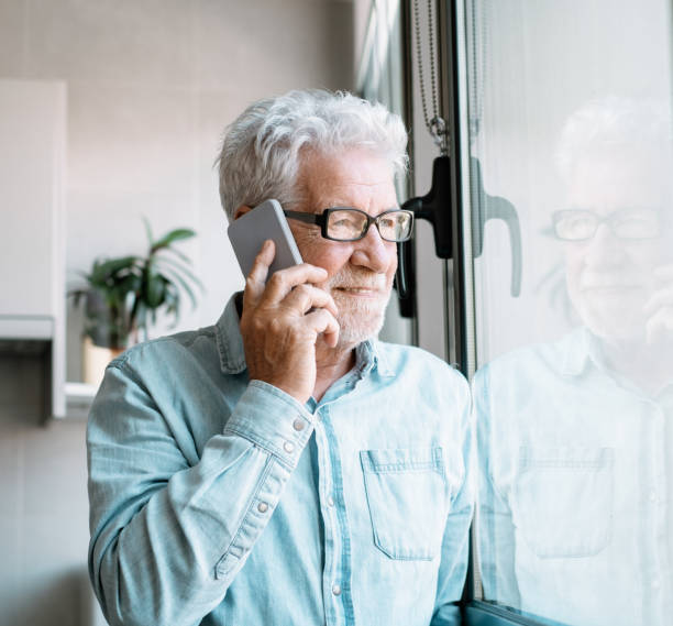 istock Handsome smiling bearded senior man looking into the distance out the window while talking on the mobile phone. 2152210046