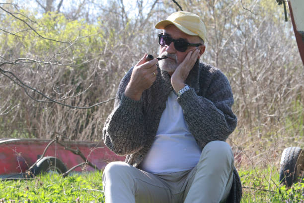Mature man, 50s, wearing yellow shirt, sunglasses and hat, sitting, posing with hands. Stylish person. Brazil