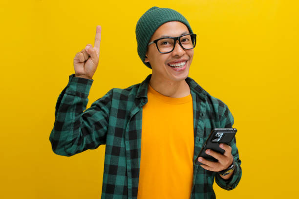 istock Asian man points at an empty space while confidently holding his phone, displaying excitement 2152210734