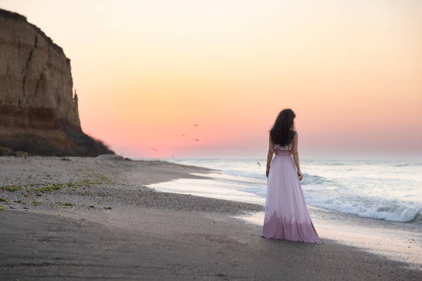Romantic and fairytale view of a wonderful sunrise at seaside and a young woman admiring and enjoying the moment.