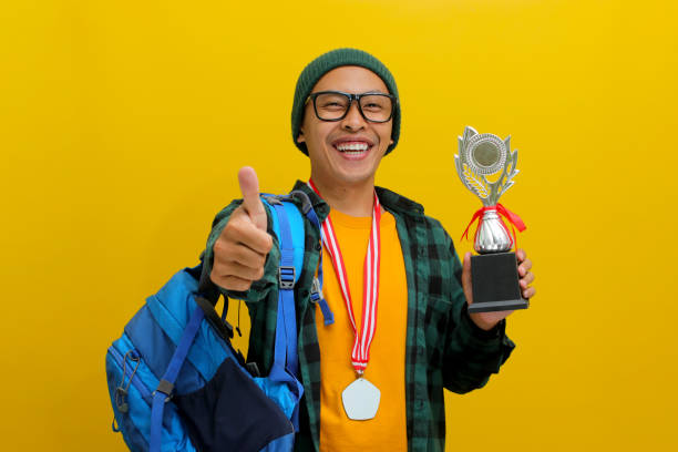 istock Excited Asian Student Gives Thumbs Up While Holding Trophy, Celebrating Success 2152217480