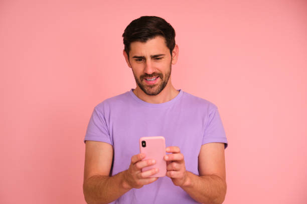 istock A man smiling and looking at his smartphone over pink background. 2152217887