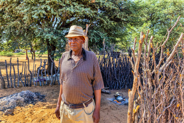 African village, senior man making tea on the open fire in the outdoors kitchen,