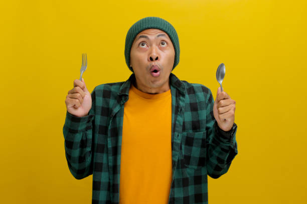 istock Excited Young Asian man looking up while holding spoon and fork, isolated on yellow background 2152220887