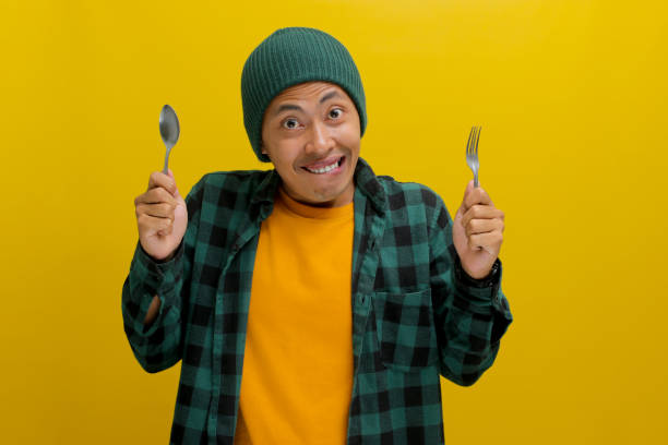 istock Hungry Asian man bites his lips while holding a fork and a spoon 2152221375