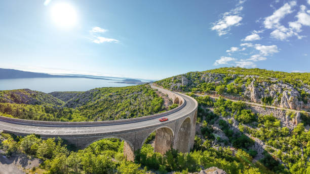 The Adriatic Highway (Croatian: Jadranska magistrala) is a road that stretches along the eastern coast of the Adriatic Sea and is part of the European route E65. Aerial view of cars driving over the large viaduct at sunset, FPV view.