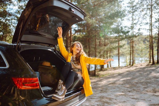 Young woman enjoying nature sitting in open trunk.