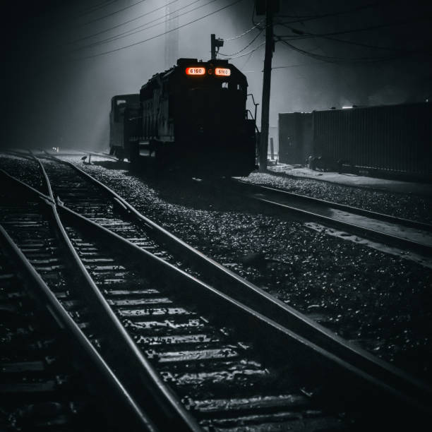 A single black  train on the tracks in a train yard in the fog at night.