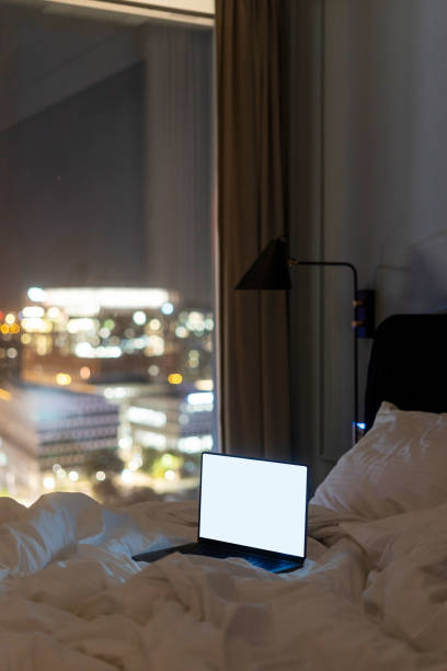 istock Laptop with empty display on bed and window with city view in cozy hotel room 2152242334