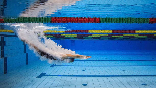 Female swimmer in water immersion phase, entering and sliding below the water surface making wonderful bubbles, underwater shot.