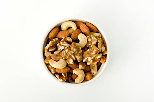 A bowl of nuts in soft focus, behind a few nuts on a white surface, with tiny nut fragnebts, Isolated on white with plenty of room for text.