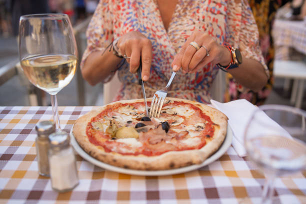 In the center of Florence, Italy, a close-up depicts a woman's hands as she expertly cuts into a delicious pizza with tableware