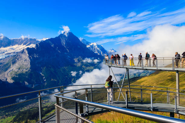 Grindelwald,  Switzerland - August 6, 2022: Tourists take photos on the First Cliff Walk, a popular viewing platform on the First mountain in Grindelwald, which offers with stunning Alpine views