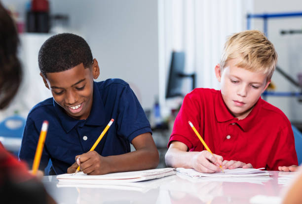 Two boys writing in class, serious and smiling Multiracial middle school students writing in class. The two middle school students are doing an assignment or taking a test. The African-American boy is smiling and his classmate has a serious expression. easy test stock pictures, royalty-free photos & images