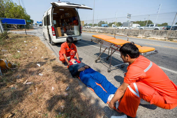 Two paramedic or emergency medical technician (EMT) in orange uniform helping neck and head accident victim lying on stretcher long spinal board. Urgent assistance during road accident.