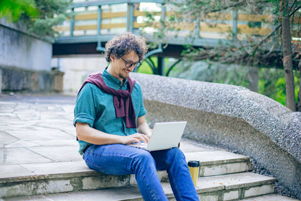 istock Smiling student sitting on stairs using laptop on coffee break 2152283716