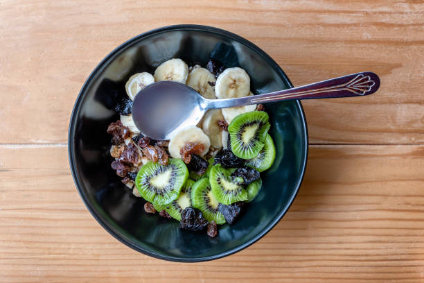Healthy breakfast. Soaked organic raw barley, walnuts, kiwi, banana, raisins, prunes and honey on the table, wooden background