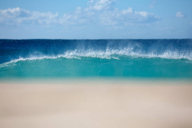 Low line view of a crystal blue wave breaking on the sand