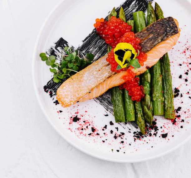 Elegant presentation of salmon with red caviar and green asparagus on a white plate