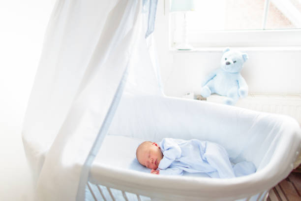 Baby playing in a white crib. Little child in bed. Bedding and furniture for kids nursery. Infant going to sleep. Nap for young kid. Sleepwear for children.