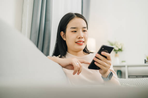 istock Happy young woman sitting on sofa use smartphone control smart lamp at home 2152287218
